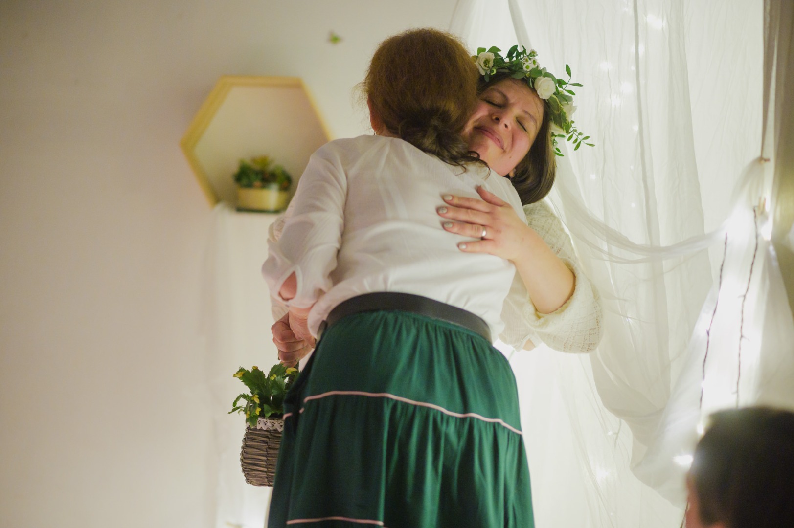 fehérbe öltözött kismama fején virágkoszorú ölelkezik